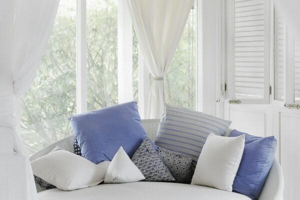 White cuddle chair with throw pillows near a window creating a luxurious feel on a budget