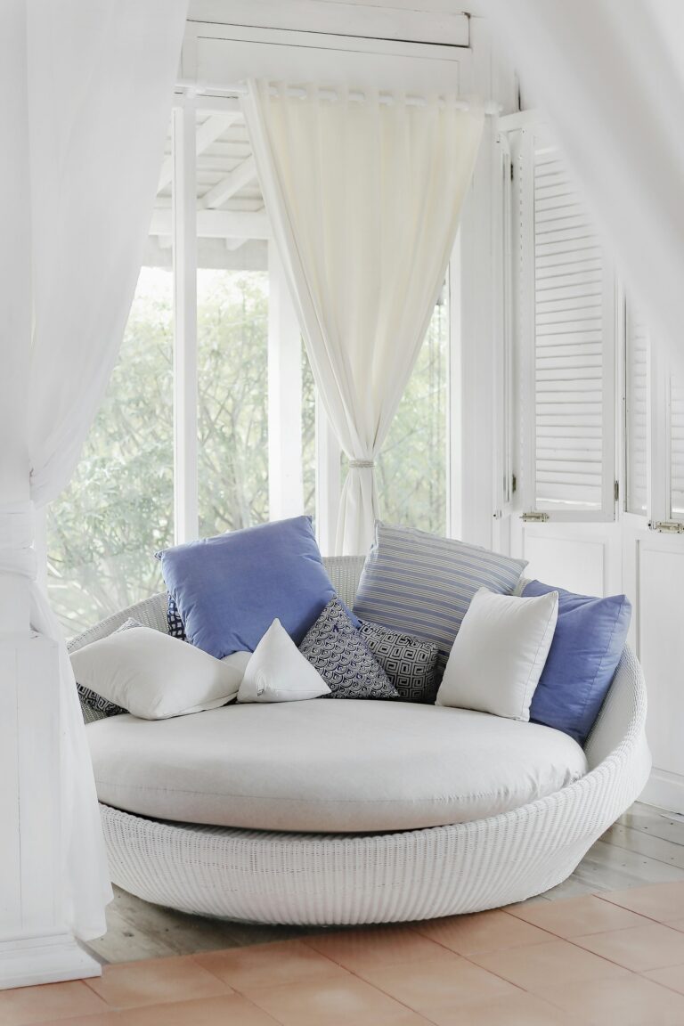 White cuddle chair with throw pillows near a window creating a luxurious feel on a budget
