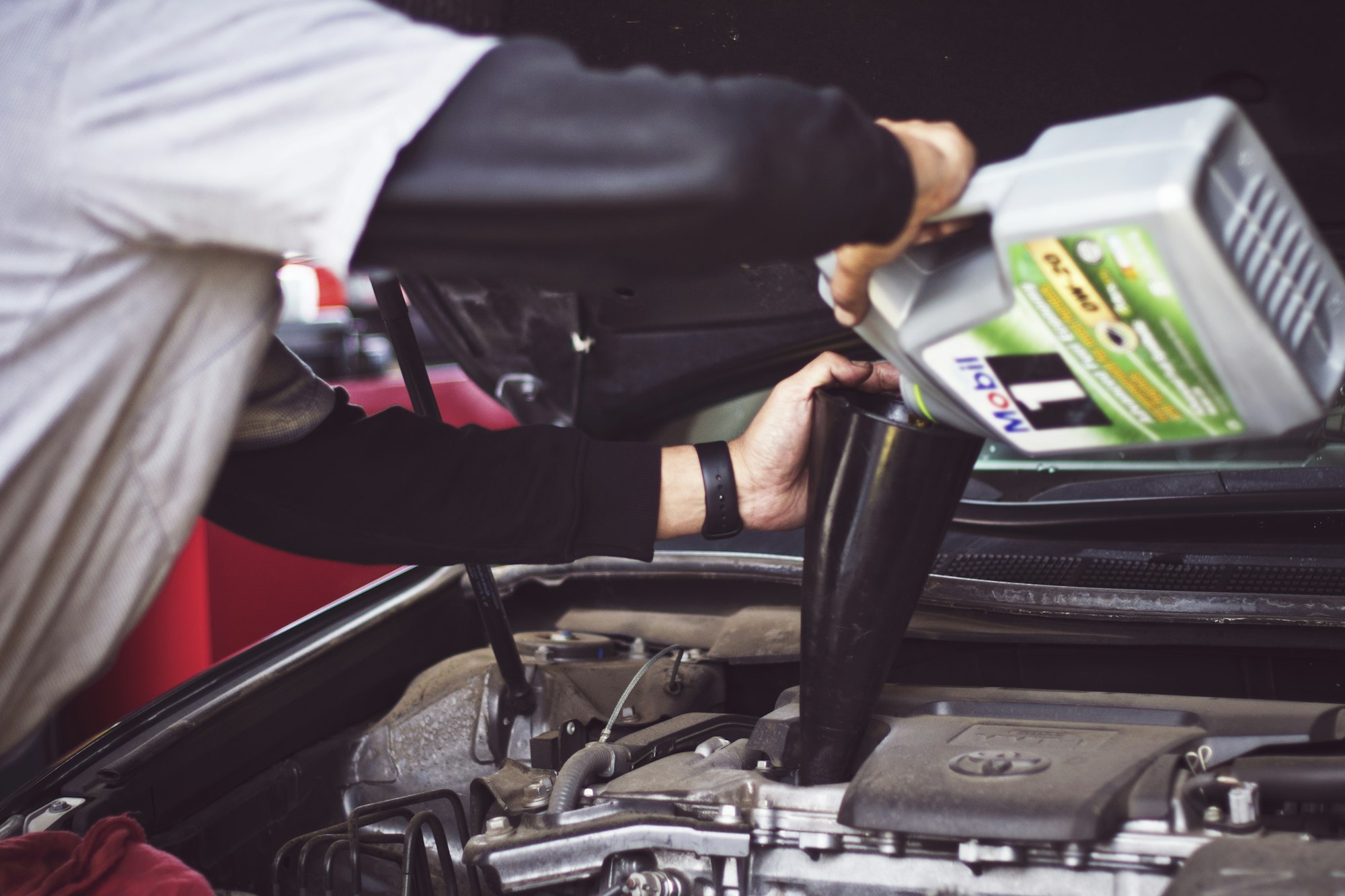 Man refilling motor oil on car engine bay for DIY maintenance